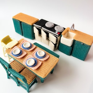 Könnte beinhalten: Ein Miniatur-Küchenspielset aus Häkelarbeit mit Herd, Spüle, Schränken und einem Esstisch mit Stühlen. Das Set ist in den Farben Grün, Gelb und Braun gehalten.