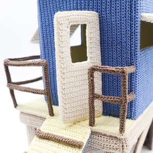 May include: A crocheted playhouse with a blue exterior, white door and brown railings. The playhouse has a yellow and beige platform with a brown railing and a yellow ramp.