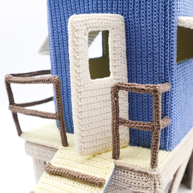 May include: A crocheted playhouse with a blue exterior, white door and brown railings. The playhouse has a yellow and beige platform with a brown railing and a yellow ramp.