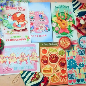 May include: A collection of Christmas greeting cards featuring illustrations of reindeer, bears, and snowmen. The cards are decorated with festive colours and patterns, including red, green, and white.
