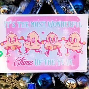 May include: A pink and blue Christmas card with four cartoon bells holding hands. The card reads "It's the most wonderful Chime of the Year".
