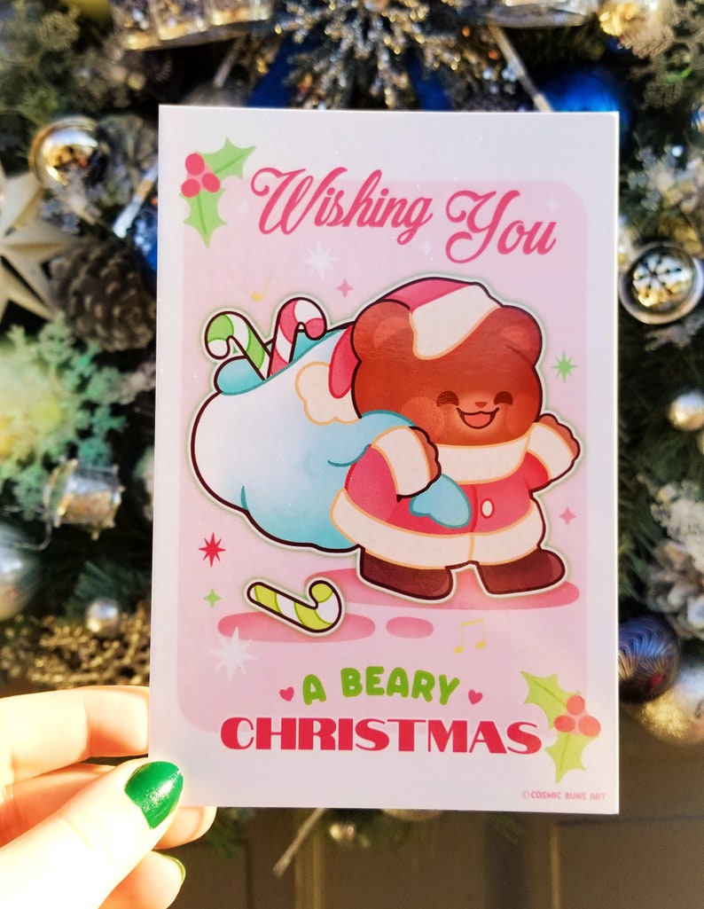 May include: A pink Christmas card with a cartoon bear wearing a Santa hat and carrying a bag of candy canes. The card says "Wishing You A Beary Christmas".