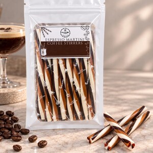 May include: A clear plastic pouch containing multiple long, thin, cylindrical coffee stirrers with a diagonal striped pattern in dark brown, light brown, and white. The label reads "ESPRESSO MARTINI COFFEE STIRRERS" with a logo and small graphic icons.