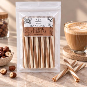 May include: A clear plastic pouch containing multiple hazelnut drink stirrers with a brown and white spiral pattern. The label features the text "HAZELNUT DRINK STIRRERS" and "COFFEE SWEET" along with illustrations of a hazelnut and a coffee cup.