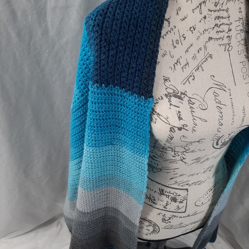 K&ouml;nnte beinhalten: Eine gestrickte Strickjacke in Blau, Grau und Wei&szlig; mit einem langen, offenen Vorderteil.