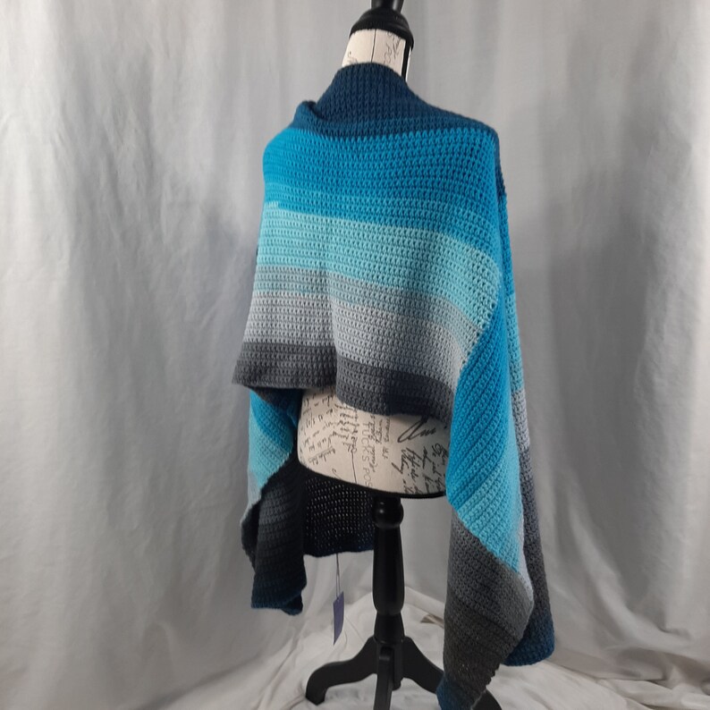 K&ouml;nnte beinhalten: Ein gestrickter Schal in den Farben Blau, Grau und Schwarz, der &uuml;ber einer Schaufensterpuppe drapiert ist.