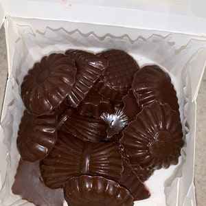 May include: A box of assorted dark chocolate sweets in various shapes, including flowers, shells, and swirls.