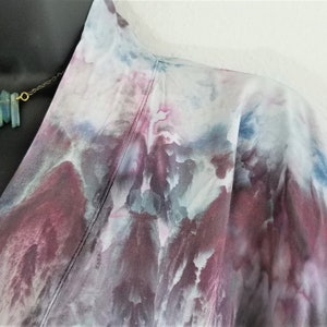 May include: A white, blue, and purple tie-dye kimono with a gold and blue gemstone necklace.