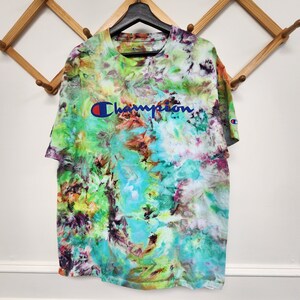 May include: A tie-dye t-shirt with a blue and white "Champion" logo on the front. The shirt is a mix of green, blue, yellow, orange, and purple.