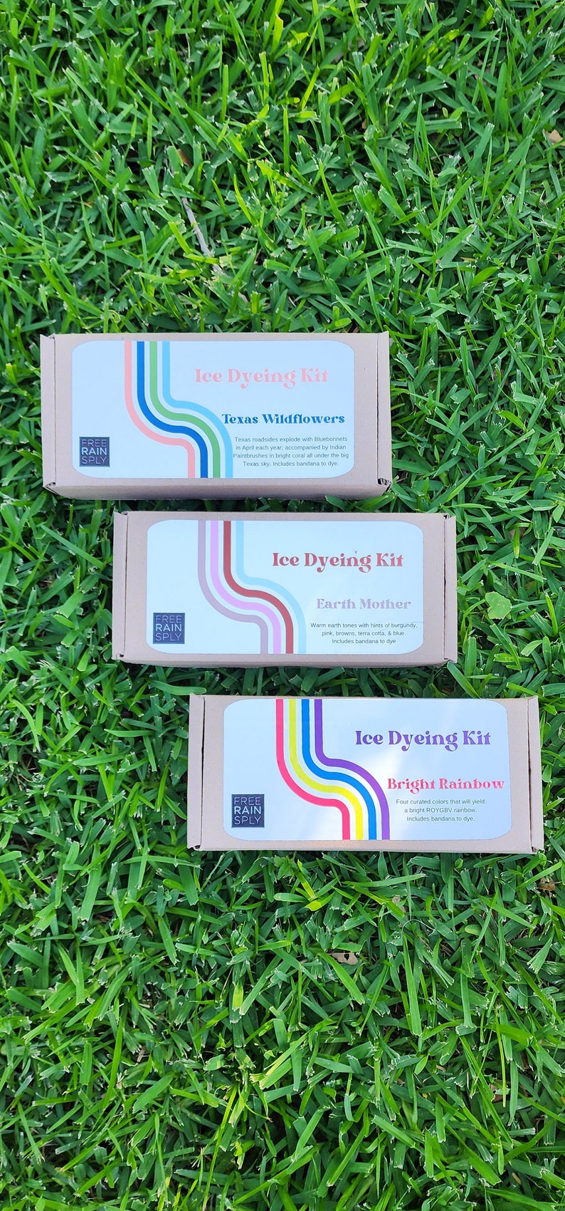 May include: Three craft kits for ice dyeing, each in a cardboard box, are displayed on green grass. The boxes have labels with colorful rainbow designs and text, including "Ice Dyeing Kit" and various color themes.
