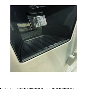 May include: A close-up of a stainless steel refrigerator water dispenser with a black drip tray. The tray is designed to catch water drips from the dispenser.