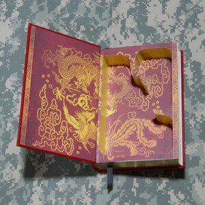 May include: Open red book with gold dragon and phoenix illustrations on the inside pages. The illustrations are set against a burgundy background. A gold ribbon bookmark and a gold ribbon are attached to the book.