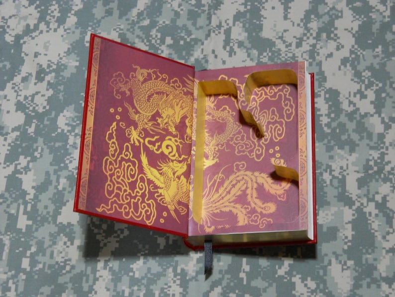 May include: Open red book with gold dragon and phoenix illustrations on the inside pages. The illustrations are set against a burgundy background. A gold ribbon bookmark and a gold ribbon are attached to the book.