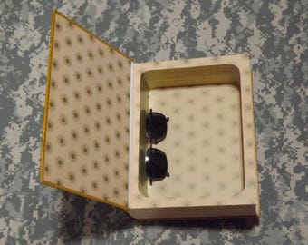 May include: A book with a hidden compartment, the compartment is open and a pair of black sunglasses are inside.