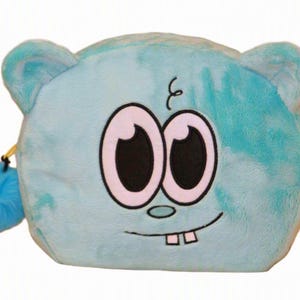 Op de afbeelding: Een lichtblauw pluche etui in de vorm van een cartoon-karakterhoofd met twee grote ogen, een kleine neus en twee zichtbare tanden. Het etui heeft een zachte, pluizige textuur, afgeronde oren en een bijpassende blauwe pompon aan de ritssluiting.