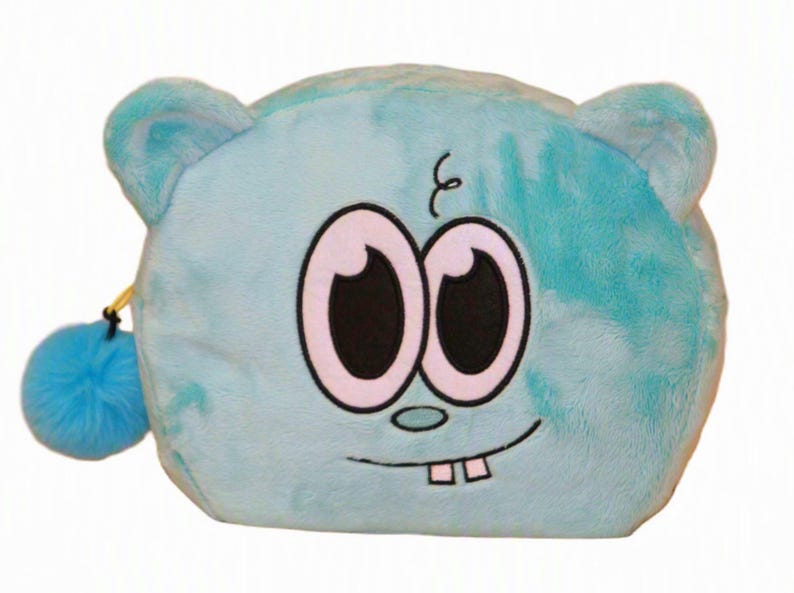 Op de afbeelding: Een lichtblauw pluche etui in de vorm van een cartoon-karakterhoofd met twee grote ogen, een kleine neus en twee zichtbare tanden. Het etui heeft een zachte, pluizige textuur, afgeronde oren en een bijpassende blauwe pompon aan de ritssluiting.