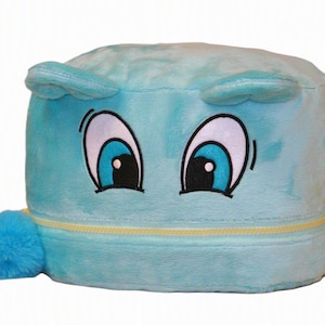 Op de afbeelding: Een lichtblauwe pluche opbergcontainer met een zachte, pluizige textuur. De voorkant is voorzien van geborduurde cartoonogen met blauwe irissen en wit oogwit. Een gele rits loopt horizontaal over het midden, met een blauwe pompon aan de ritstrekker.