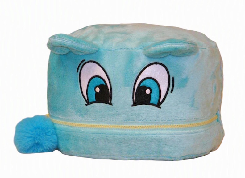 Op de afbeelding: Een lichtblauwe pluche opbergcontainer met een zachte, pluizige textuur. De voorkant is voorzien van geborduurde cartoonogen met blauwe irissen en wit oogwit. Een gele rits loopt horizontaal over het midden, met een blauwe pompon aan de ritstrekker.