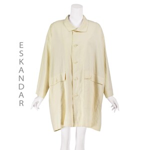 May include: A light yellow coat with a collared neckline, button-down front, and two front pockets. The coat is displayed on a mannequin. The word "ESKANDAR" is printed vertically on the left side of the coat.