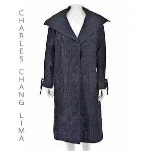 Puede incluir: Un abrigo largo negro con un patrón texturizado, un cuello grande y detalles de lazos en las mangas. El abrigo se exhibe en un maniquí. El texto "CHARLES CHANG LIMA" está impreso verticalmente a la izquierda.