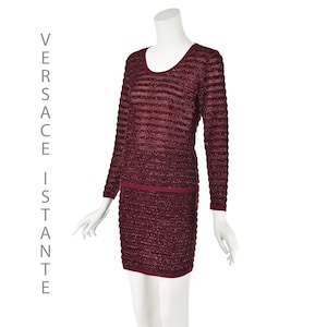 May include: A burgundy-colored, two-piece outfit on a mannequin. The long-sleeved top and matching skirt feature horizontal stripes. The text "VERSACE ISTANTE" is printed vertically on the left side of the image.