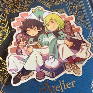 Könnte beinhalten: Ein Aufkleber mit zwei Anime-Charakteren, die zusammen sitzen und jeweils ein Buch halten. Sie tragen weiße und grüne Outfits, einer mit braunen Haaren, der andere blond. Der Aufkleber befindet sich auf einem blauen Hintergrund mit goldenem Text.
