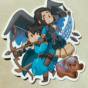 May include: A sticker featuring two cartoon characters, one with black wings and a blue outfit, the other with a blue outfit and a bow and arrow. The characters are standing on a brown bear plush toy.