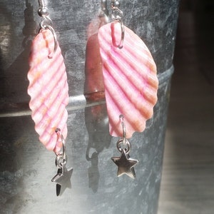 May include: A pair of pink seashell earrings with silver star charms hanging from them.