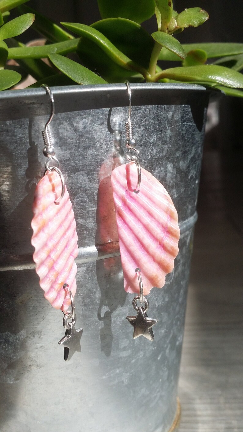 May include: A pair of pink seashell earrings with silver star charms hanging from them.