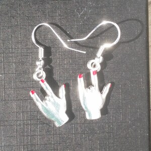 May include: A pair of silver earrings in the shape of hands making the rock and roll hand gesture. The fingernails are painted red. The earrings have a hook closure.