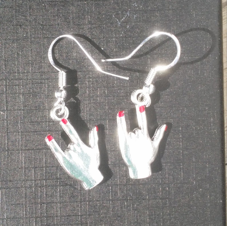 May include: A pair of silver earrings in the shape of hands making the rock and roll hand gesture. The fingernails are painted red. The earrings have a hook closure.