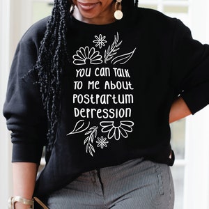 Puede incluir: Sudadera negra con texto blanco y diseño floral que dice "Puedes hablar conmigo sobre la depresión posparto."