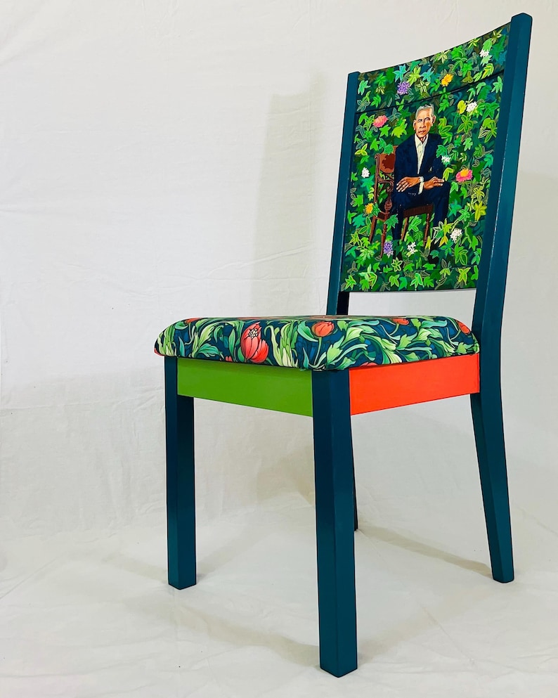 Puede incluir: Una silla azul verdosa con un asiento estampado en verde, rojo y naranja. El respaldo de la silla est&aacute; cubierto con un patr&oacute;n floral verde con un retrato de un hombre en el centro.