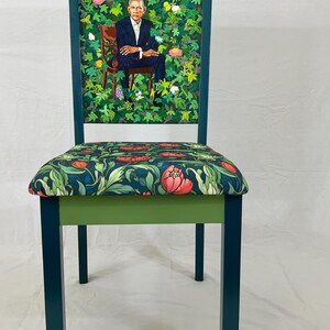Puede incluir: Una silla azul verdosa con un asiento estampado floral verde y un respaldo verde con una pintura de un hombre con traje sentado en un jard&iacute;n.