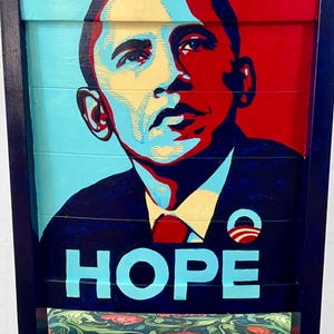 Puede incluir: Una silla de madera pintada con un retrato de Barack Obama, la palabra "HOPE" en azul y un patr&oacute;n floral en el asiento.