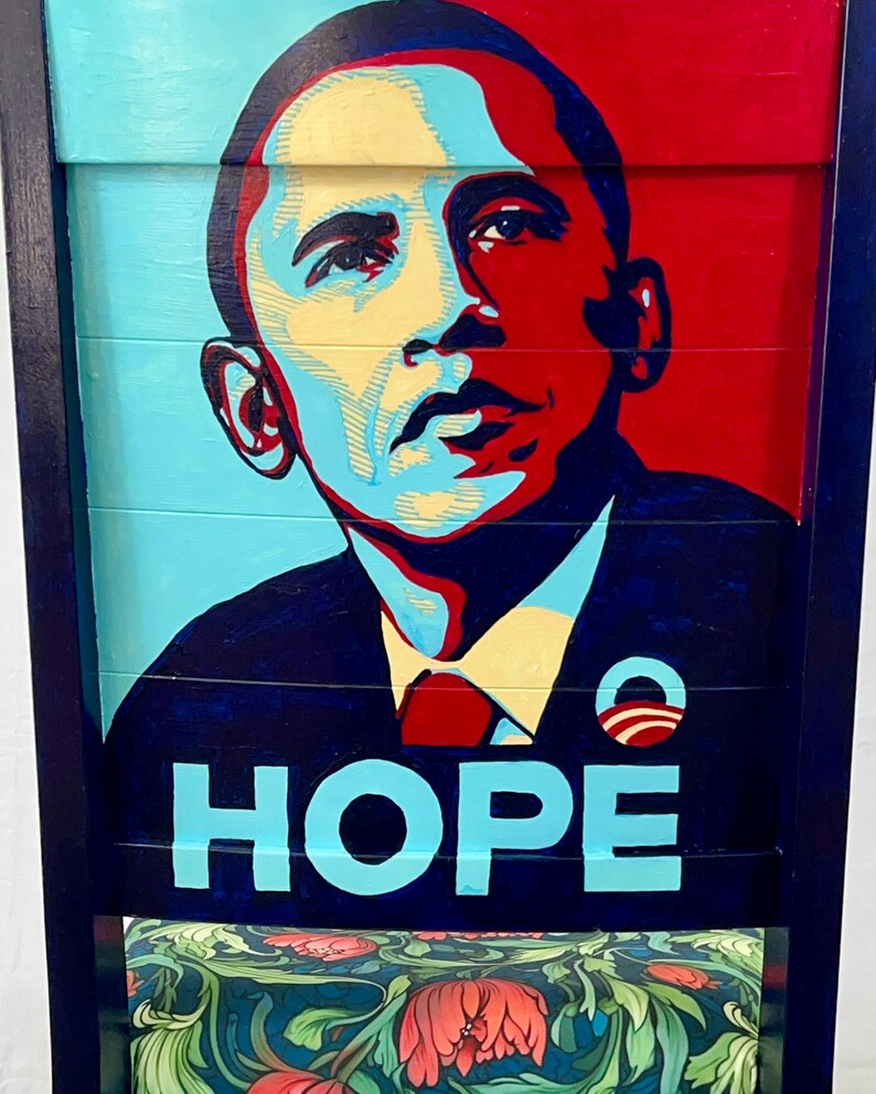 Puede incluir: Una silla de madera pintada con un retrato de Barack Obama, la palabra "HOPE" en azul y un patr&oacute;n floral en el asiento.