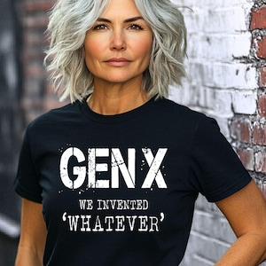 Puede incluir: Camiseta negra con el texto blanco "GENX WE INVENTED 'WHATEVER'". La camiseta la lleva una persona con pelo corto y gris, apoyada en una pared de ladrillo. El diseño de la camiseta es una declaración audaz.