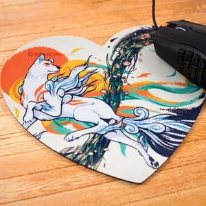 May include: Heart-shaped mousepad featuring a white wolf with red markings, set against a vibrant orange and yellow sun. The design includes blue, green, and white accents, with the text "@FRIUNICORNSSTUDIO". A black computer mouse rests on the pad.