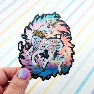 May include: A sticker featuring a white unicorn with a rainbow mane and tail. The unicorn is wearing a crown of thorns and the text "TRAMPLE BIGOTRY" is written on a speech bubble coming from its mouth.