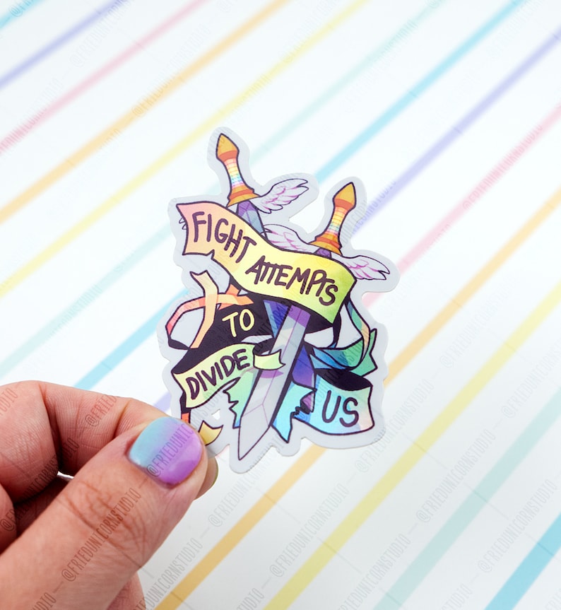 May include: A rainbow-coloured sticker with two swords crossed over each other. The swords are wrapped in a banner that reads "Fight Attempts to Divide Us".