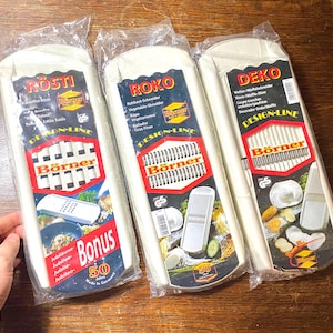 May include: Three white and red vegetable slicers in plastic packaging. Each package features the "Börner" brand name and product information. The slicers are labeled "Rosti", "Roko", and "Deko" with additional text.