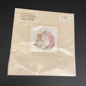 May include: An old print of a watercolor illustration featuring a cat in a blue outfit and a cat in a pink dress. The print is in a cream-colored mat with text that reads "TOM KITTEN was very fort, and he had goowej; several buttons bast off. Beatrix Potter."