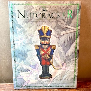 May include: A hardback book titled "The Nutcracker" with a colourful illustration of a nutcracker soldier. The cover features a winter scene with fairies and the text "A Young Reader's Edition of the Holiday Classic". Illustrated by Don Daily.