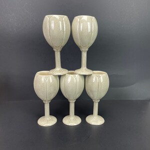 May include: Six speckled, light-colored ceramic wine glasses. The glasses are stacked in a pyramid shape, with two glasses on top of four. Each glass has a tulip-shaped bowl and a ribbed stem.