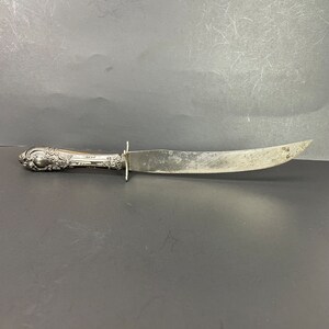 May include: A silver knife with a curved blade. The handle features an ornate, floral pattern. The knife shows signs of wear, suggesting it is vintage or antique.