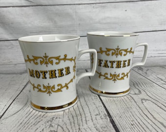 Peut inclure: Deux tasses en céramique blanche avec des bordures et des poignées dorées. L'une porte l'inscription "MOTHER" et l'autre "FATHER" en lettres dorées. Les deux tasses présentent des motifs décoratifs dorés.