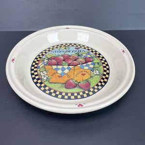 May include: Cream ceramic serving bowl with a strawberry design. The centre features a box of strawberries with the words "STRAWBERRIES" and "FRESH FRUIT". The rim has small red hearts and a checkered border. A charming piece for serving.