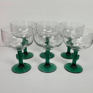 Puede incluir: Seis copas de margarita transparentes con tallos verdes en forma de cactus. Las copas tienen un cuenco redondeado y una base ancha. El diseño de los tallos es original y decorativo.