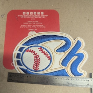 May include: Embroidered baseball patch featuring a baseball with red stitching and the letters "OH" in blue and gold. The patch is approximately 4 inches wide. A red card with text is visible in the background.