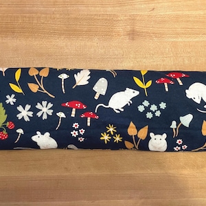 May include: A navy blue rectangular pillow with a whimsical pattern of white mice, red mushrooms, and yellow and orange foliage. The pillow has a white tag on the side.